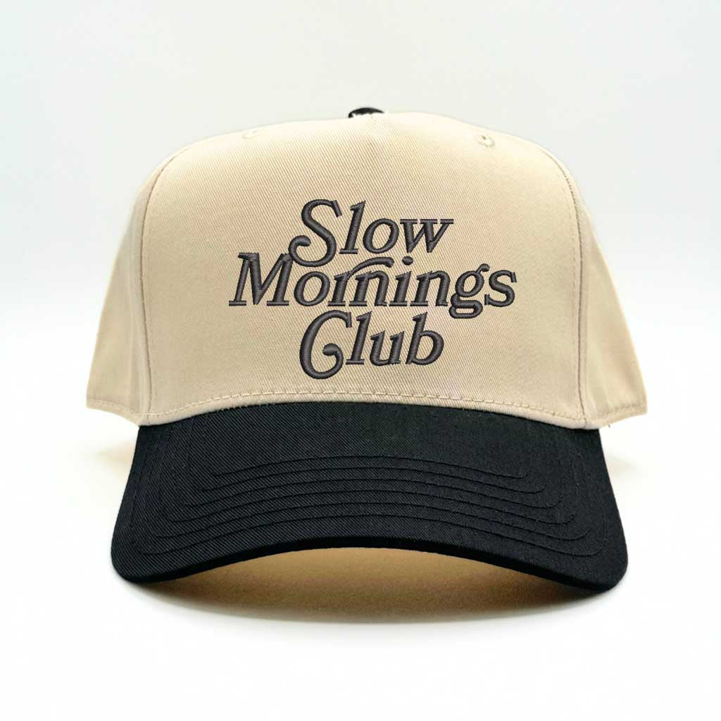 Beige and black 5-panel baseball hat with &quot;Slow Mornings Club&quot; embroidered by DSY Lifestyle in black on the front.