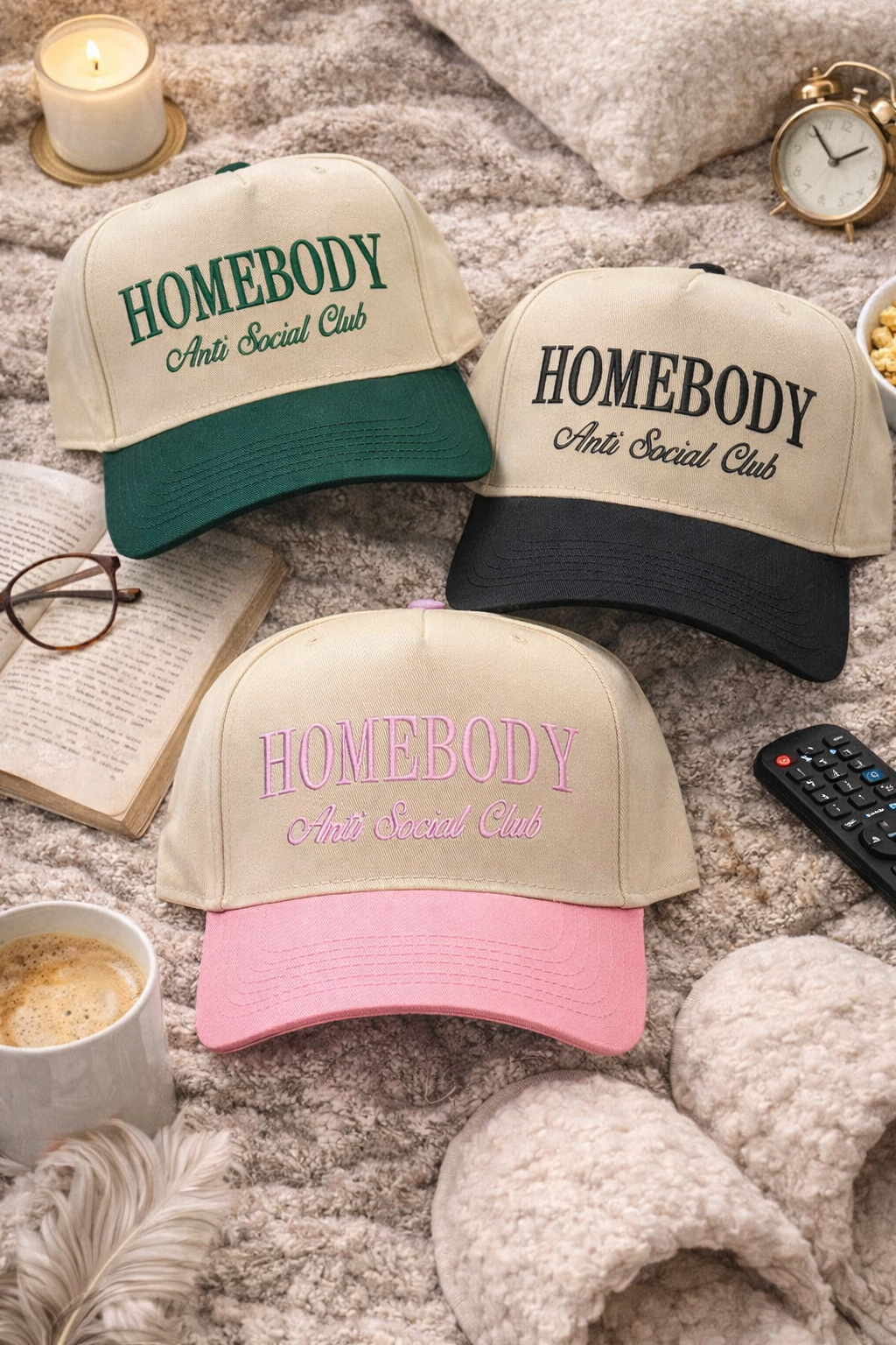 Flat lay with cozy home essentials of Natural Forest Green, Natural Black and Natural Pink Homebody Anti-Social Club embroidered baseball hats. A two-tone statement hat for women who love comfort, style, and effortless outfits. -DSY Lifestyle