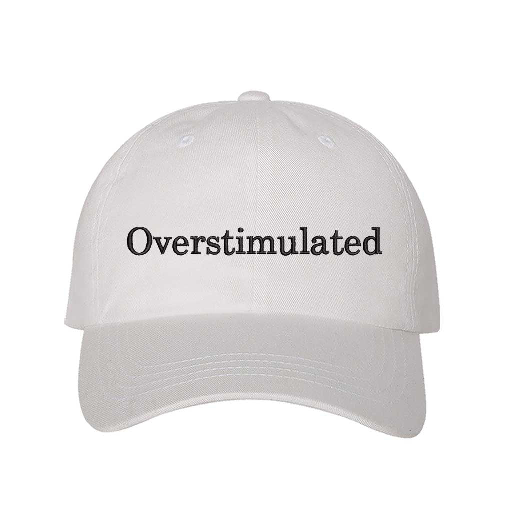 White DSY Lifestyle soft cotton baseball hat with the word Overstimulated embroidered in clean, minimalist lowercase lettering across the front. - DSY Lifestyle