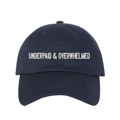 Navy blue baseball hat with the phrase underpaid &amp; overwhelmed embroidered on it-DSY Lifestyle