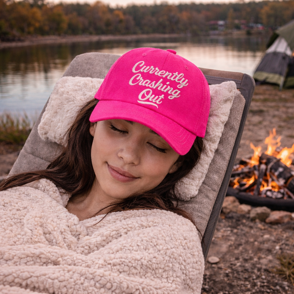 Female relaxing nap by the campfire wearing a Hot Pink Currently Crashing Out embroidered baseball hat. A statement baseball hat for women who love humor, comfort, and effortless everyday outfits. - DSY Lifestyle