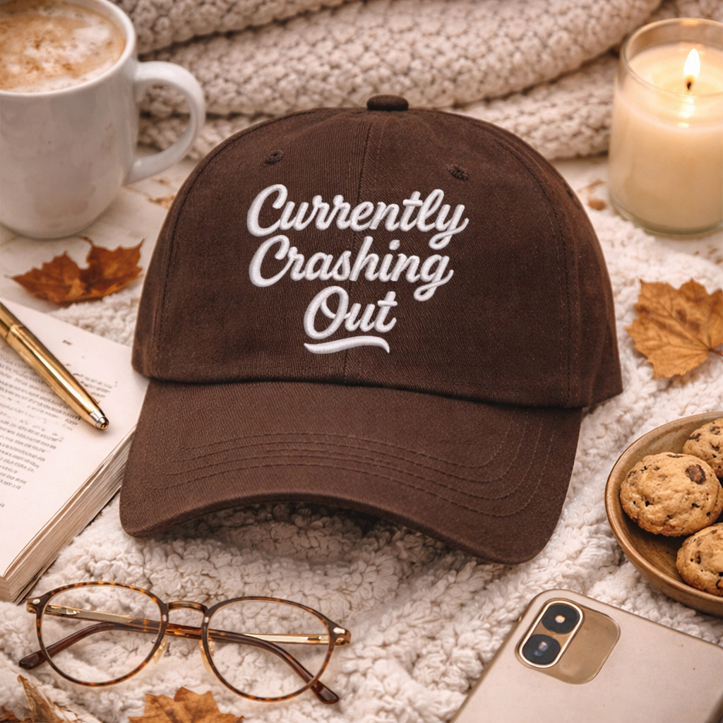 Flat lay of Brown Currently Crashing Out embroidered baseball hat. A statement baseball hat for women who love humor, comfort, and effortless everyday outfits. - DSY Lifestyle