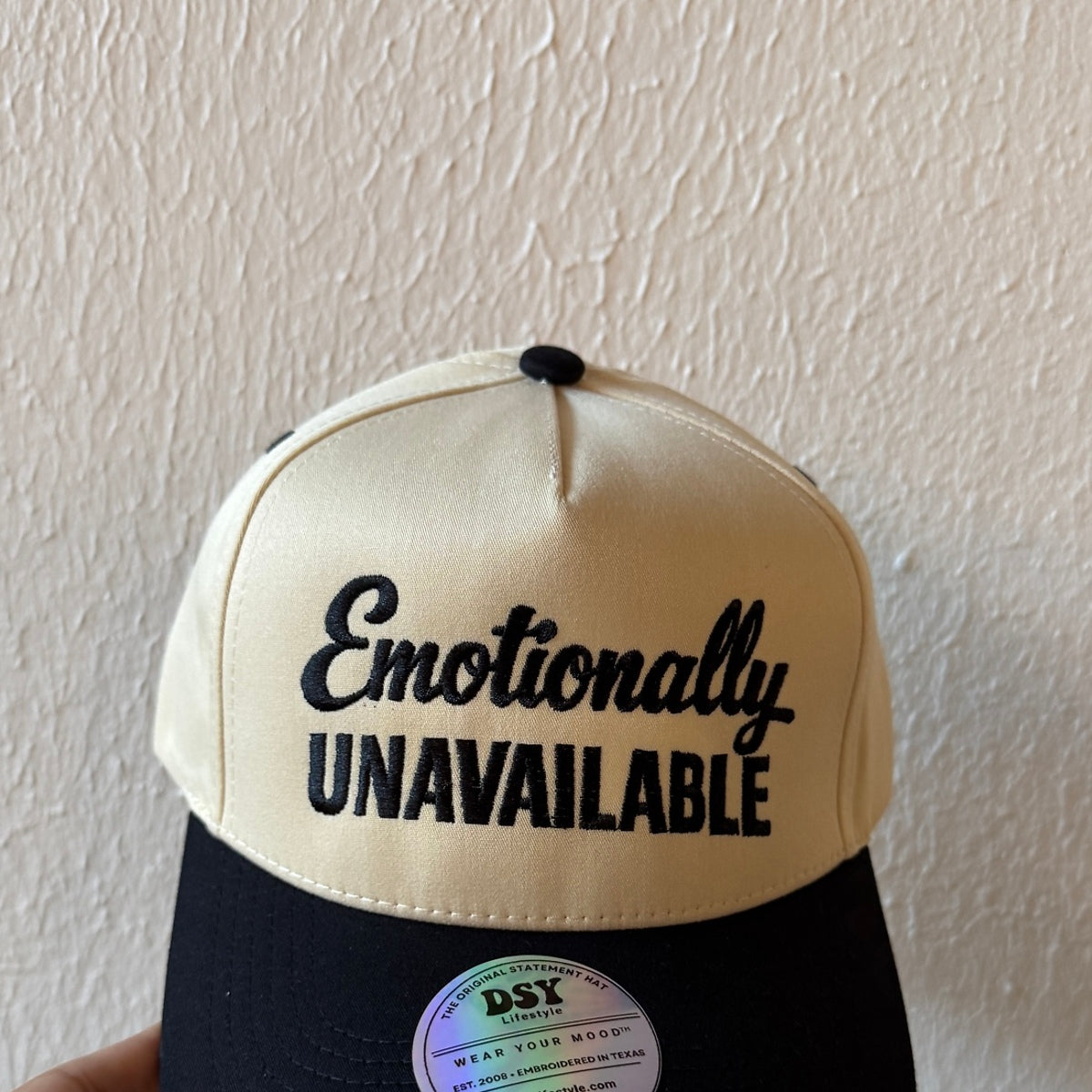 Close-up of Emotionally Unavailable machine embroidery on a two-tone trucker hat