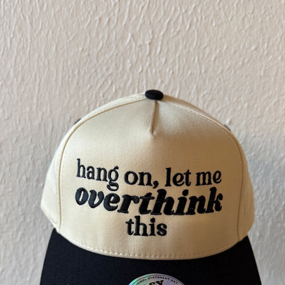 Close-up of Hang On, Let Me Overthink This machine embroidery on a two-tone trucker hat