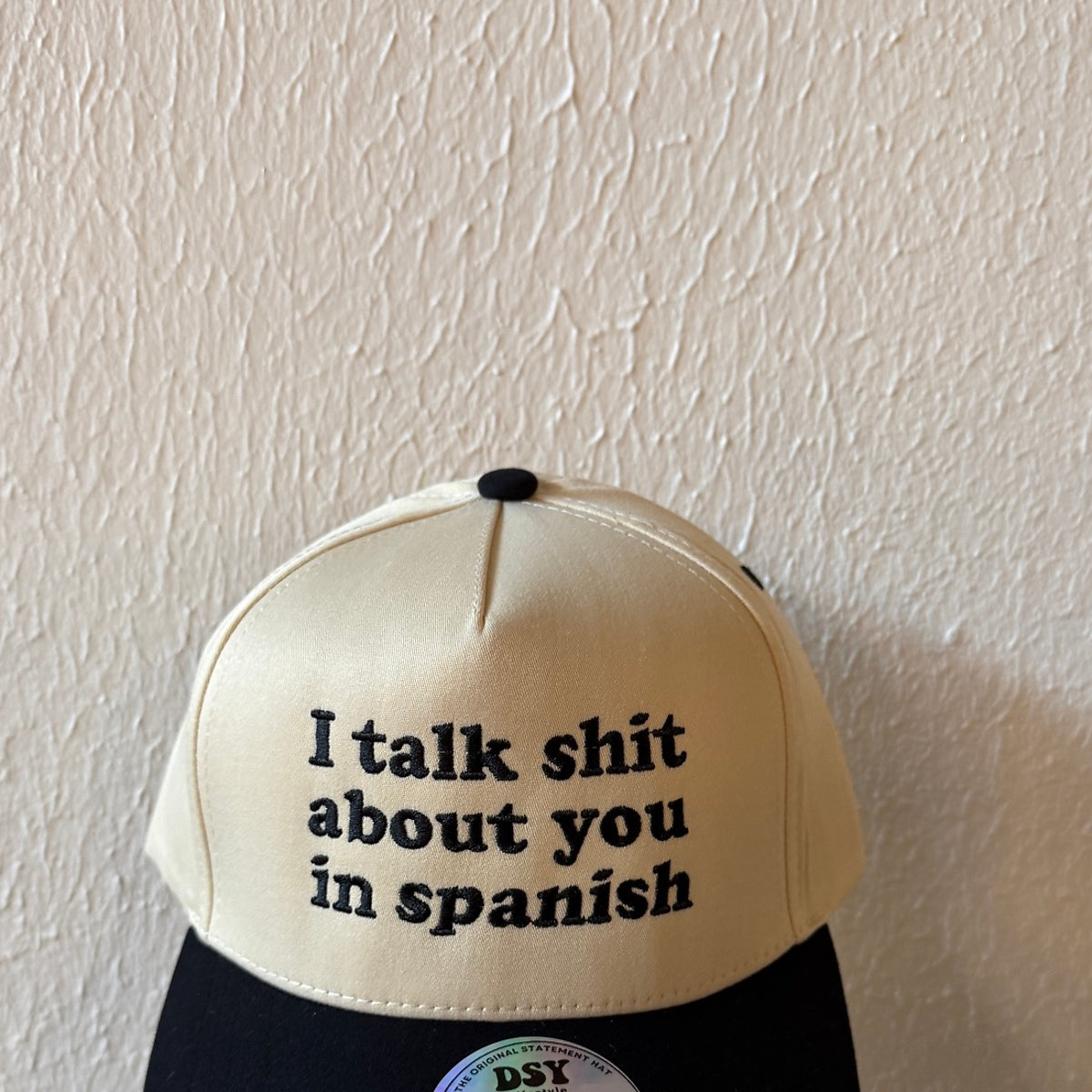 Close-up of I Talk Shit About You in Spanish machine embroidery on a two-tone trucker hat