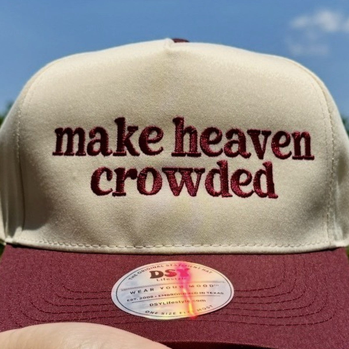 Close-up of the maroon lowercase make heaven crowded embroidery on a natural five-panel trucker hat