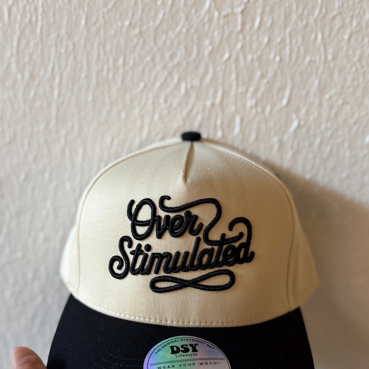 Close-up of Over Stimulated machine embroidery on a two-tone trucker hat