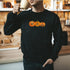 Male drinking coffee wearing a black crewneck sweatshirt printed with 3 smiling pumpkins - DSY Lifestyle