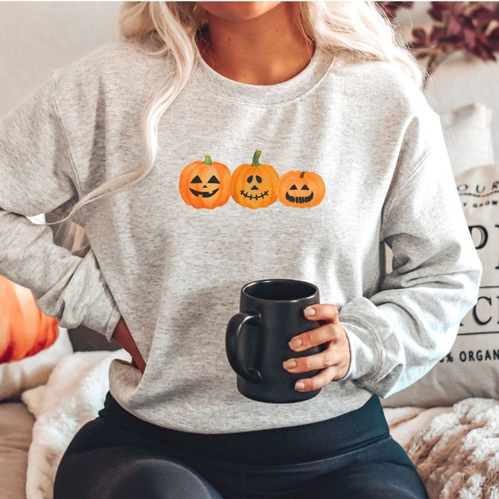 Female wearing a heather gray crewneck sweatshirt printed with 3 smiling pumpkins in the front - DSY Lifestyle