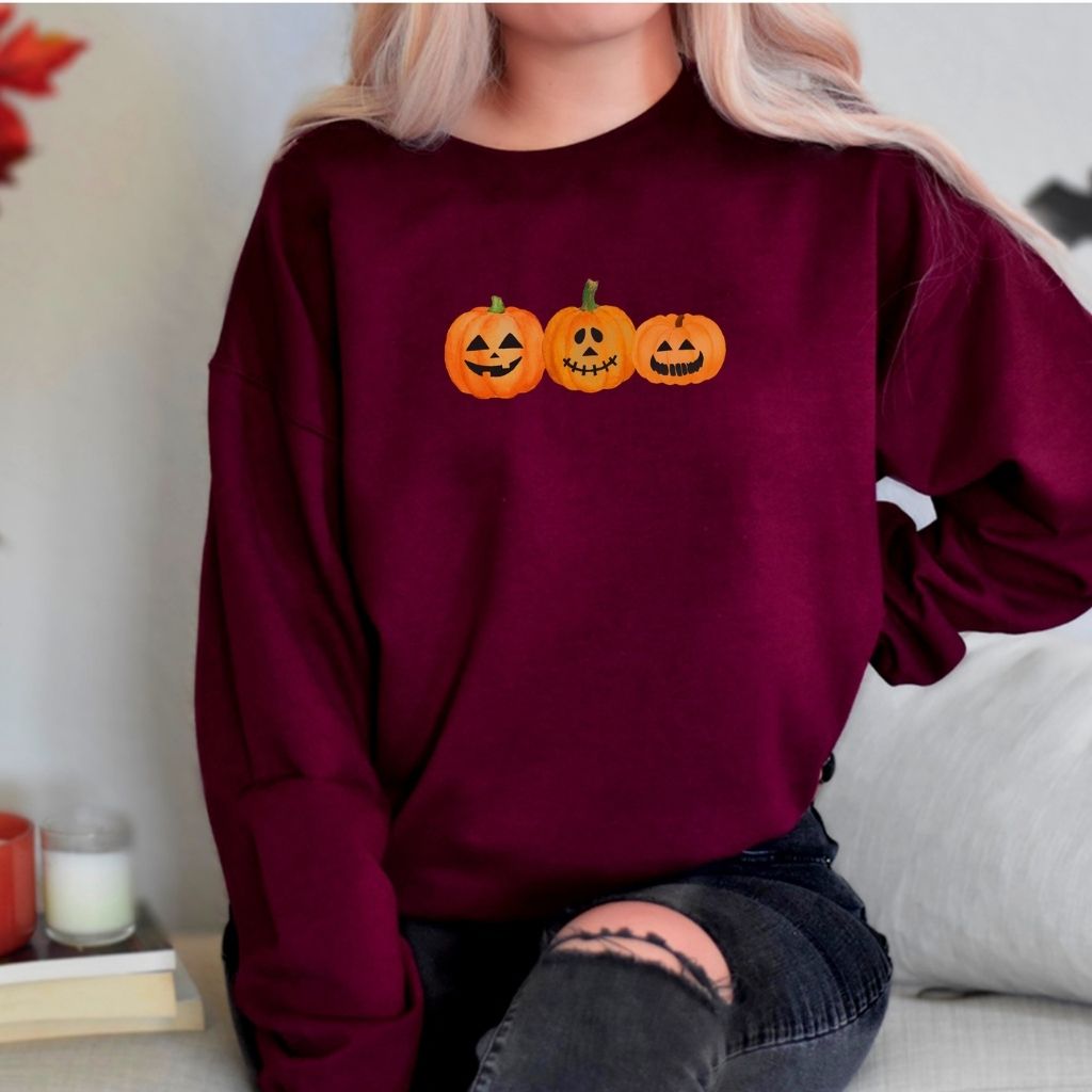 Female wearing a maroon crewneck sweatshirt printed with 3 smiling pumpkins in the front - DSY Lifestyle