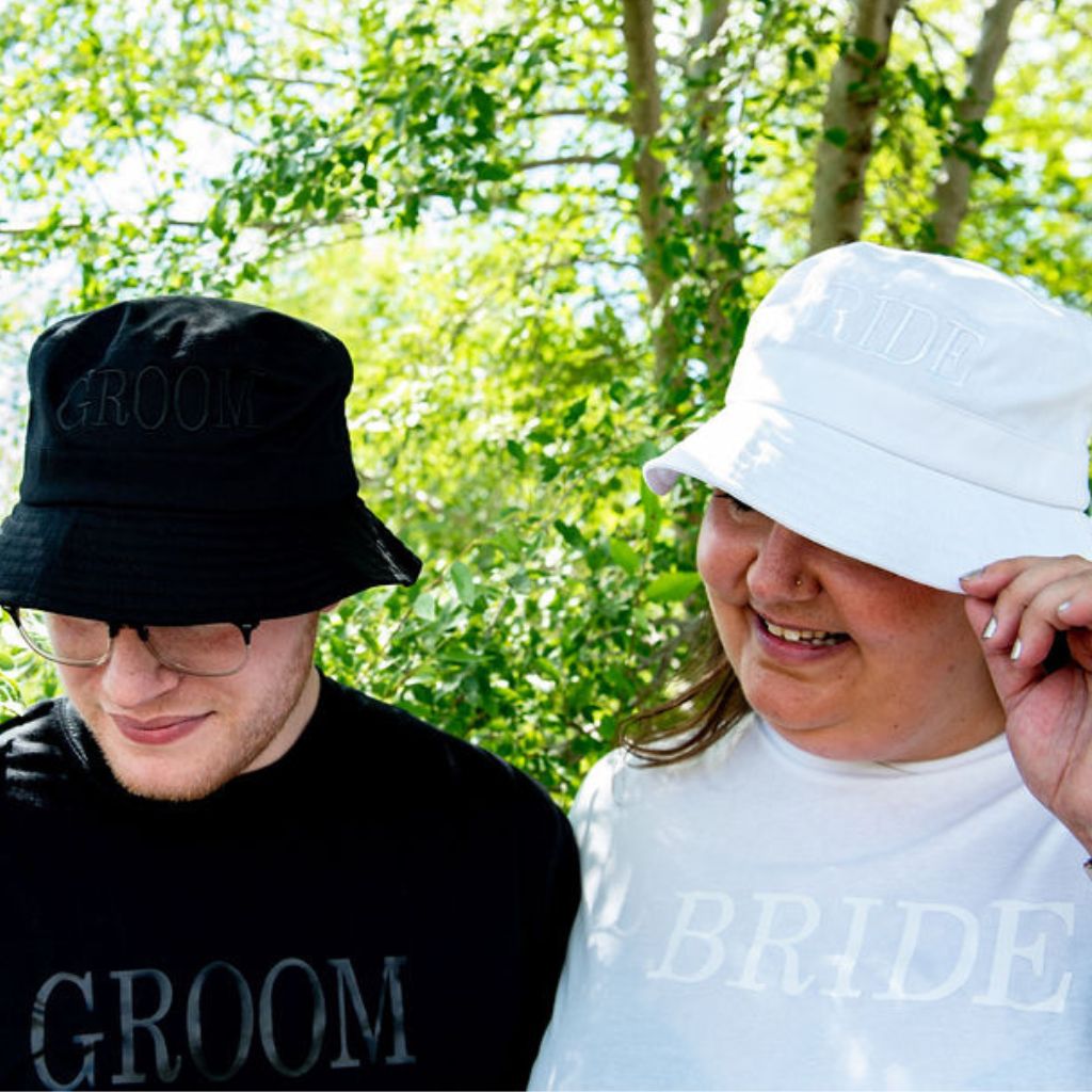 Male wearing a black hat embroidered with Groom in black thread and aFemale wearing a white bucket hat embroidered with Bride in white thread - DSY Lifestyle