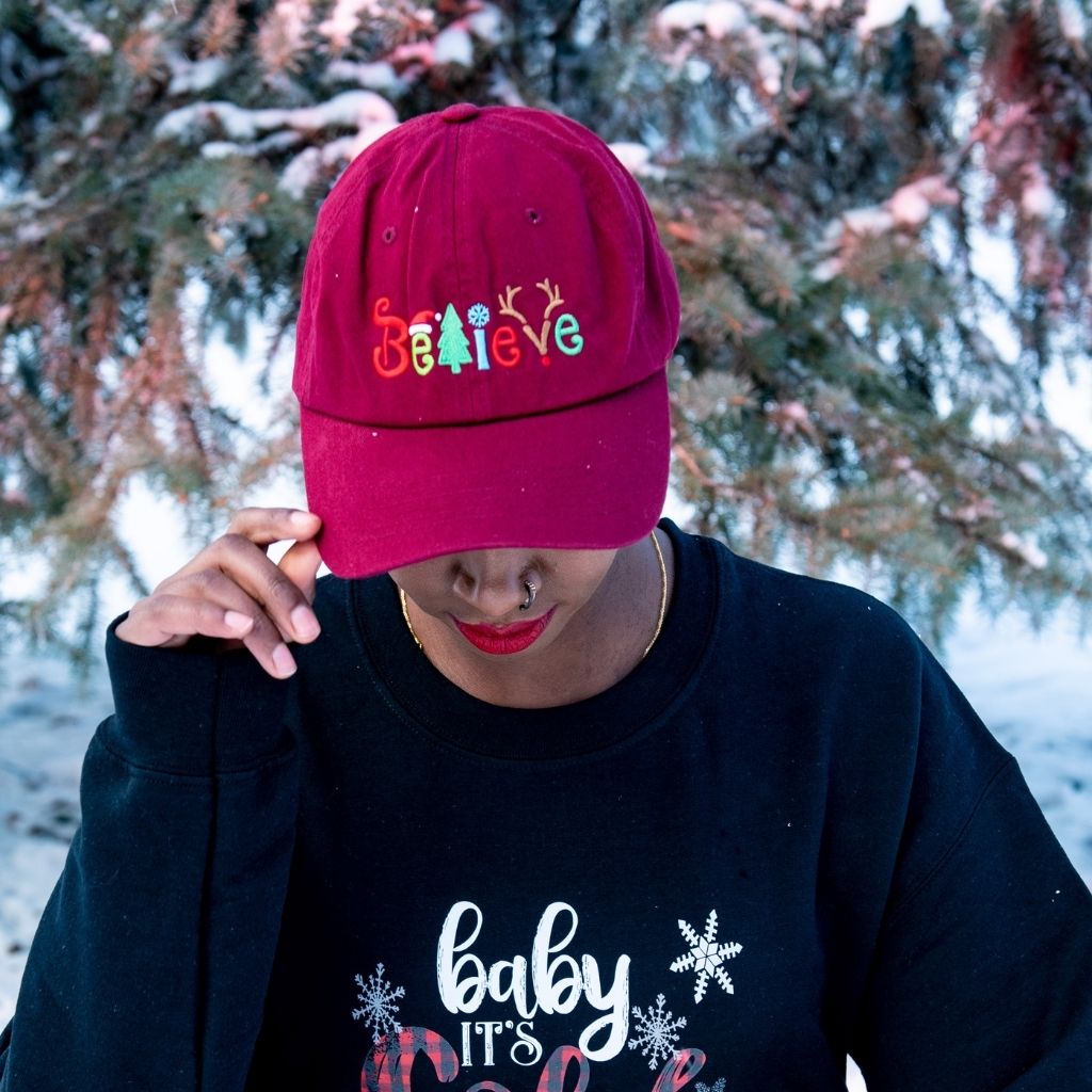 Female in the snow wearing a burgundy baseball hat embroidered with Believe in the front - DSY Lifestyle