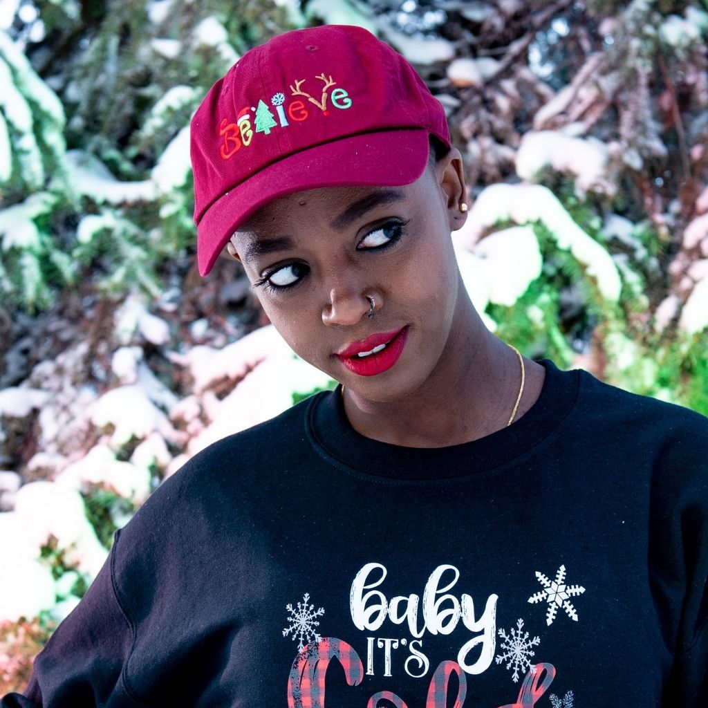 Female in the snow wearing a burgundy baseball hat embroidered with Believe in the front - DSY Lifestyle