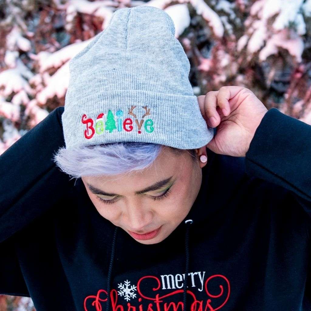 Model wearing light heather grey cuffed beanie with Believe embroidered with Christmas symbols - DSY Lifestyle