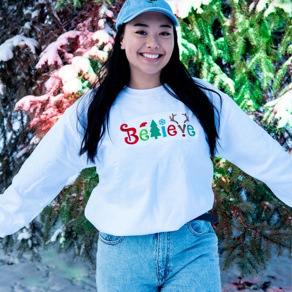 Female wearing white sweatshirt embroidered with believe in Christmas Colors- DSY Lifestyle