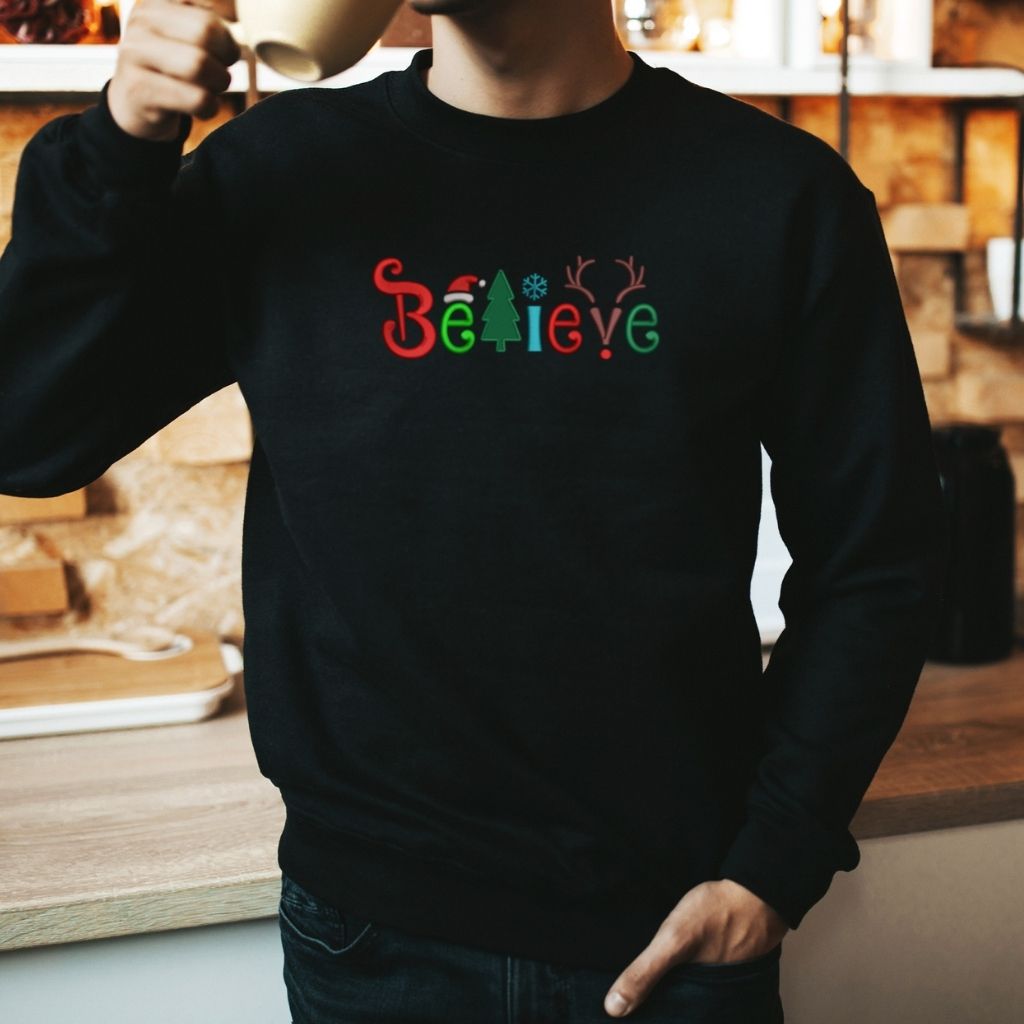 Male wearing black sweatshirt embroidered with believe in Christmas Colors- DSY Lifestyle