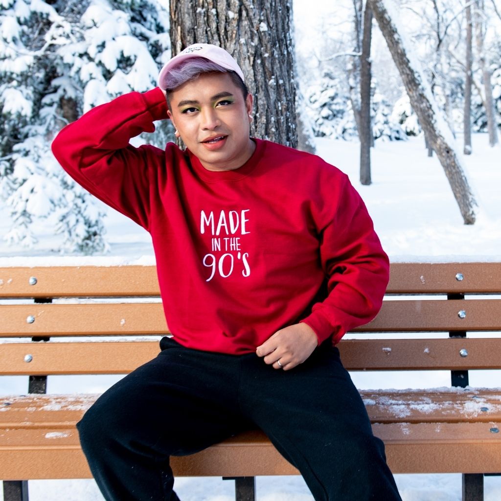 Male sitting in bench in snow wearing a cardinal embroidered sweatshirt with Made in the 90&