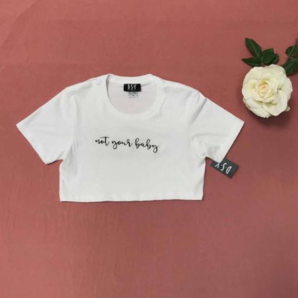 Flat lay of white underboob crop top with not your baby printed in black on the front - DSY Lifestyle