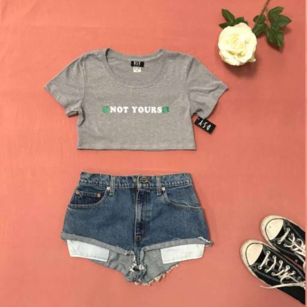 Flat lay of heather grey crop top with not yours printed on the front paired with jean shorts and sneakers - DSY Lifestyle