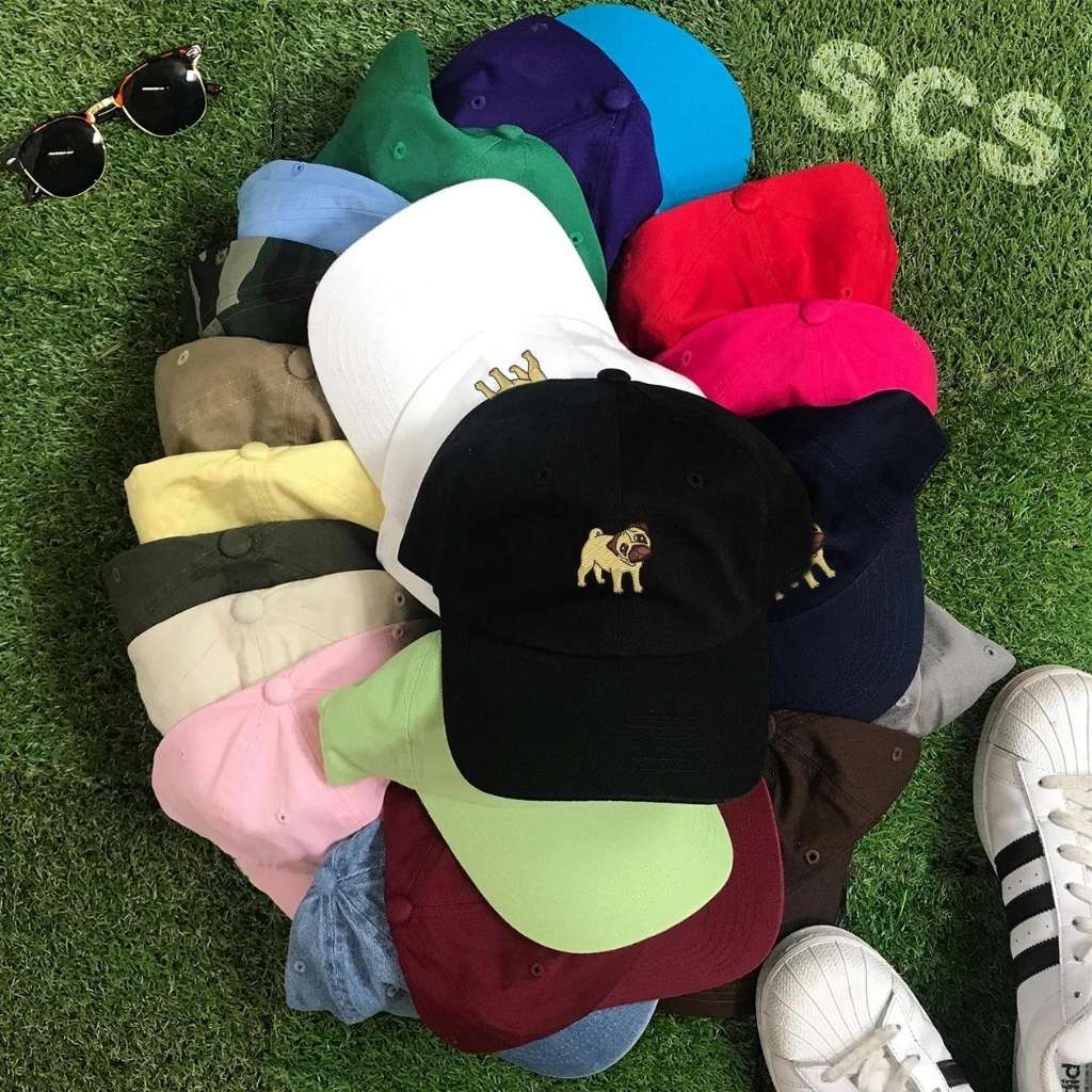 Group photo of a variety of colored baseball hats with pug embroidered